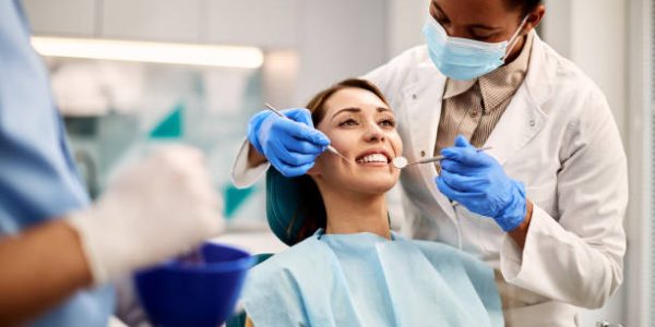 Smiling woman getting her teeth checked by African American dentist at dental clinic.
